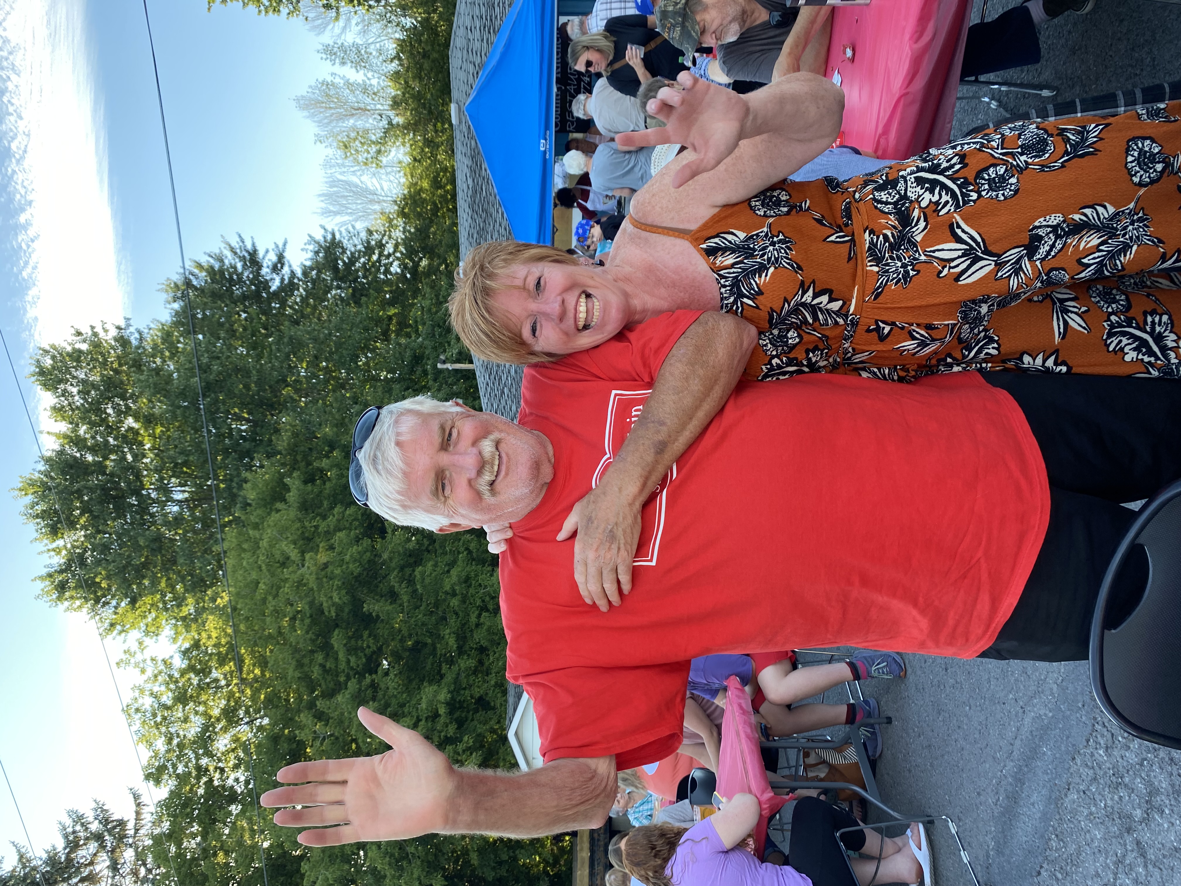 Guests in red shirt and dress standing and waving at MMOMS