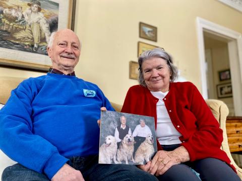 Barb and Tom Savary hold a photo of three of their golden retrievers.
