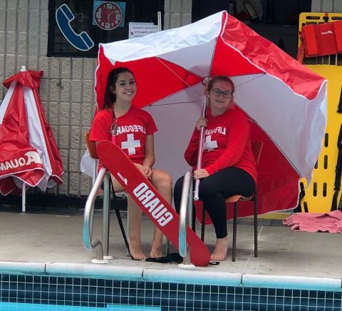 Two life guards sitting on chairs beside pool